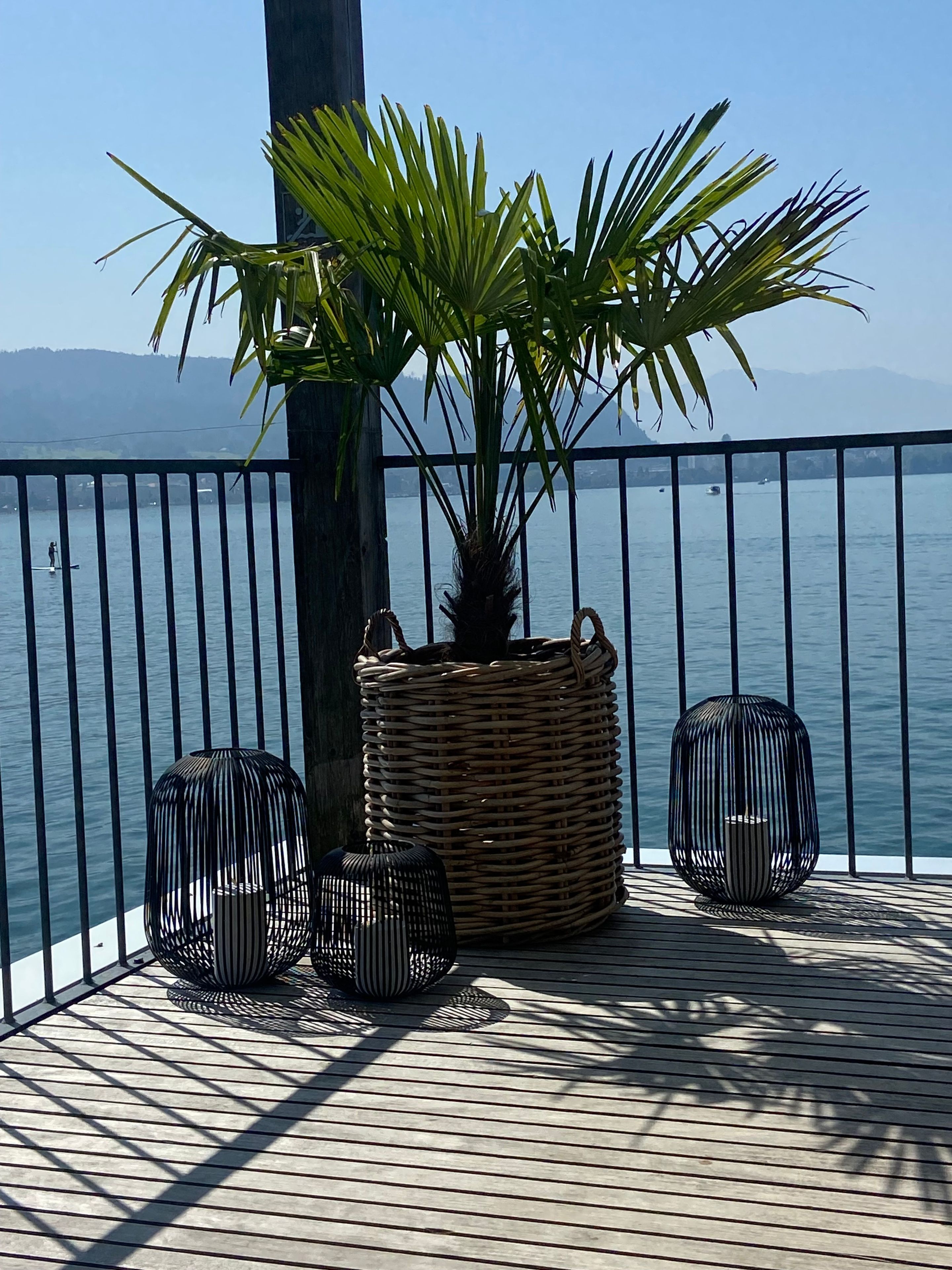 Ein Balkon mit einem Korbuschrank, zwei schwarzen Vogelkäfigen und Blick auf das Wasser.