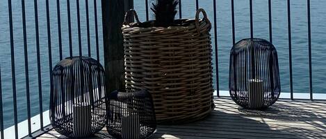 Een balkon met een rieten plantenbak, twee zwarte vogelkooien en uitzicht op het water.