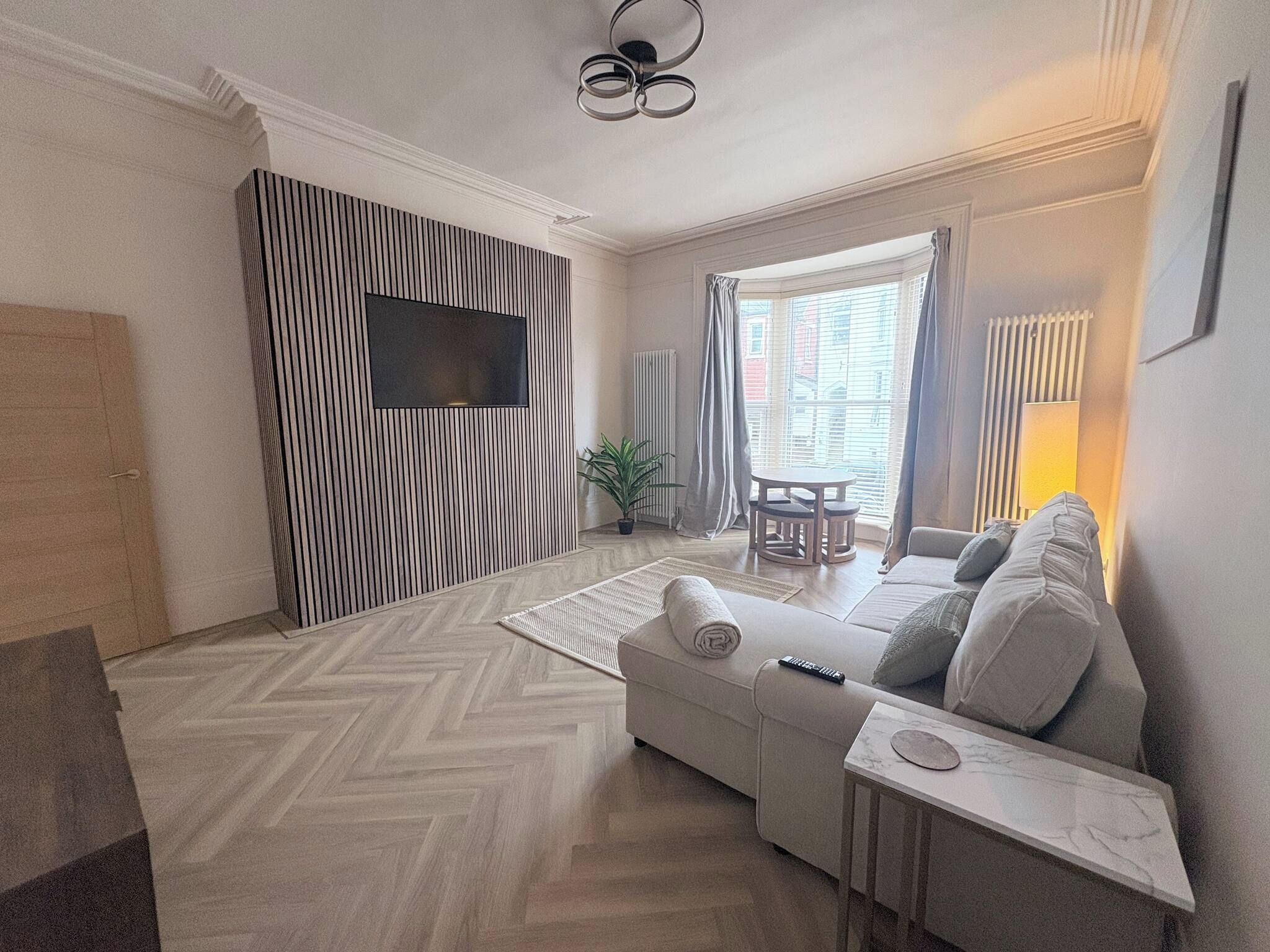 A modern living room with a sofa, a coffee table, a TV mounted on a wall, and a window with curtains.