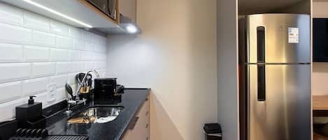 A modern kitchen with a stainless steel refrigerator, black countertop, and white tiled backsplash.