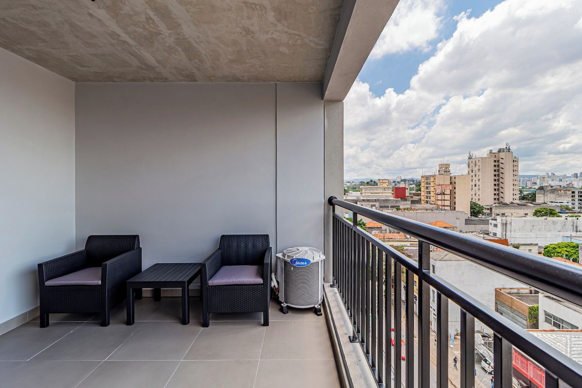 A balcony with two wicker chairs, a small table, and a waste bin.
