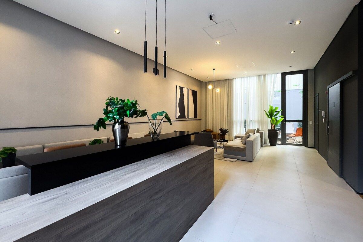 Een moderne receptie met een donker aanrecht, potplanten en een zithoek met een bank en stoelen.