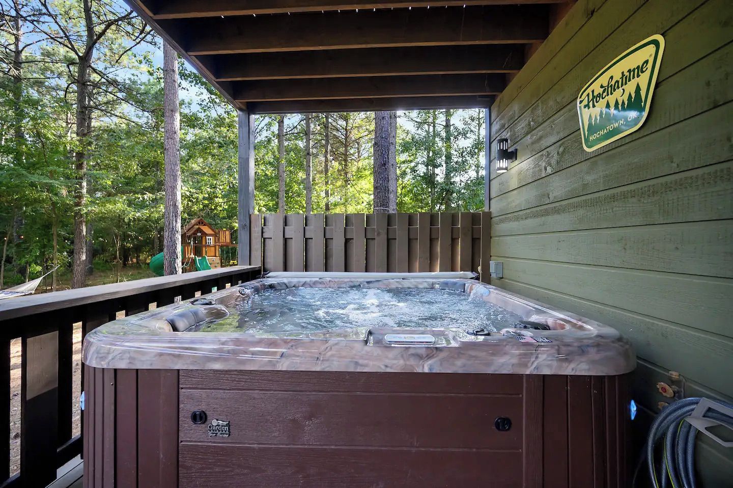 A hot tub on a wooden deck with a wooden fence and trees in the background.