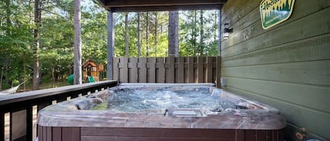 A hot tub on a wooden deck with a wooden fence and trees in the background.