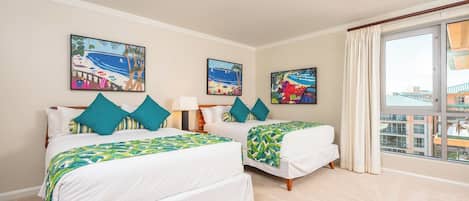 Une chambre d’hôtel avec deux lits, un ventilateur de plafond, de grandes fenêtres avec des rideaux et des œuvres d’art accrochées aux murs.