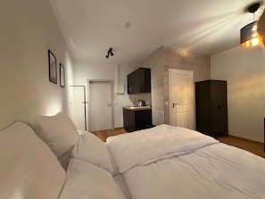 Un dormitori amb llit, petita cuina i porta que condueix a una altra habitació.