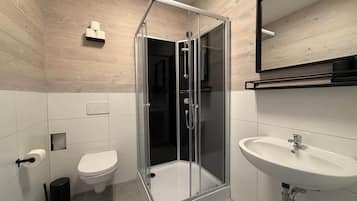 Een moderne badkamer met een douche met glazen wand, een toilet, een wastafel en een spiegel.