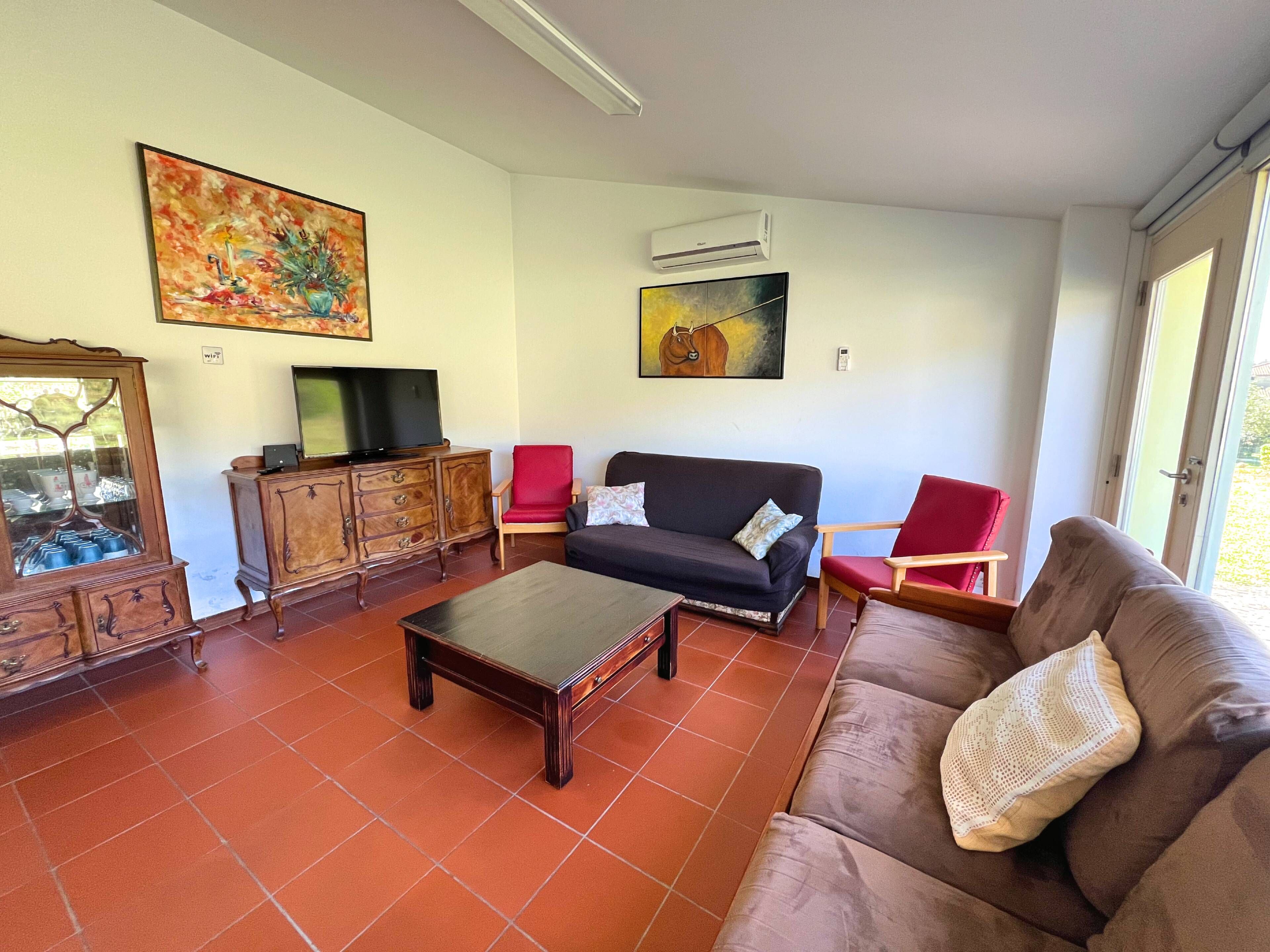 A living room with a sofa, armchairs, a coffee table, a TV on a wooden cabinet, and a painting on the wall.