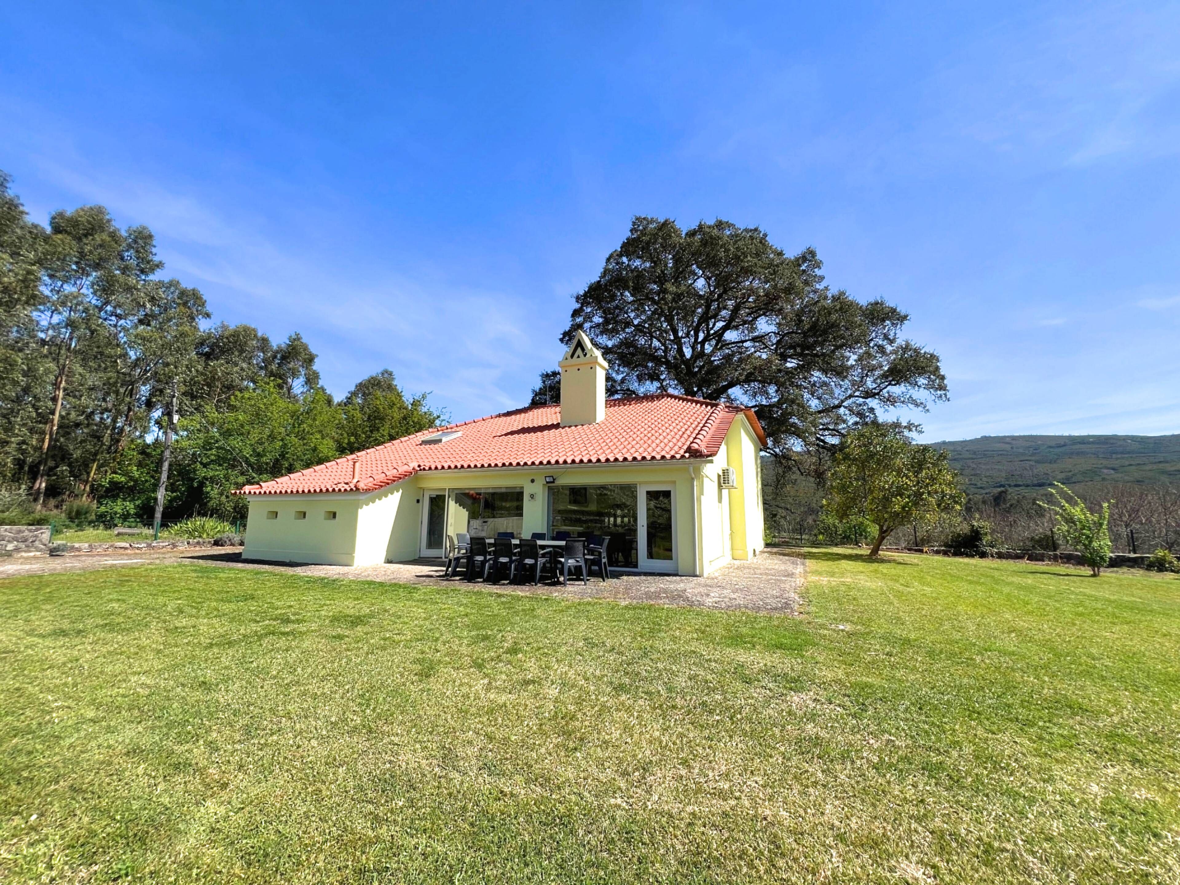 A single-story house with a red-tiled roof, a patio with outdoor furniture, and a grassy yard.