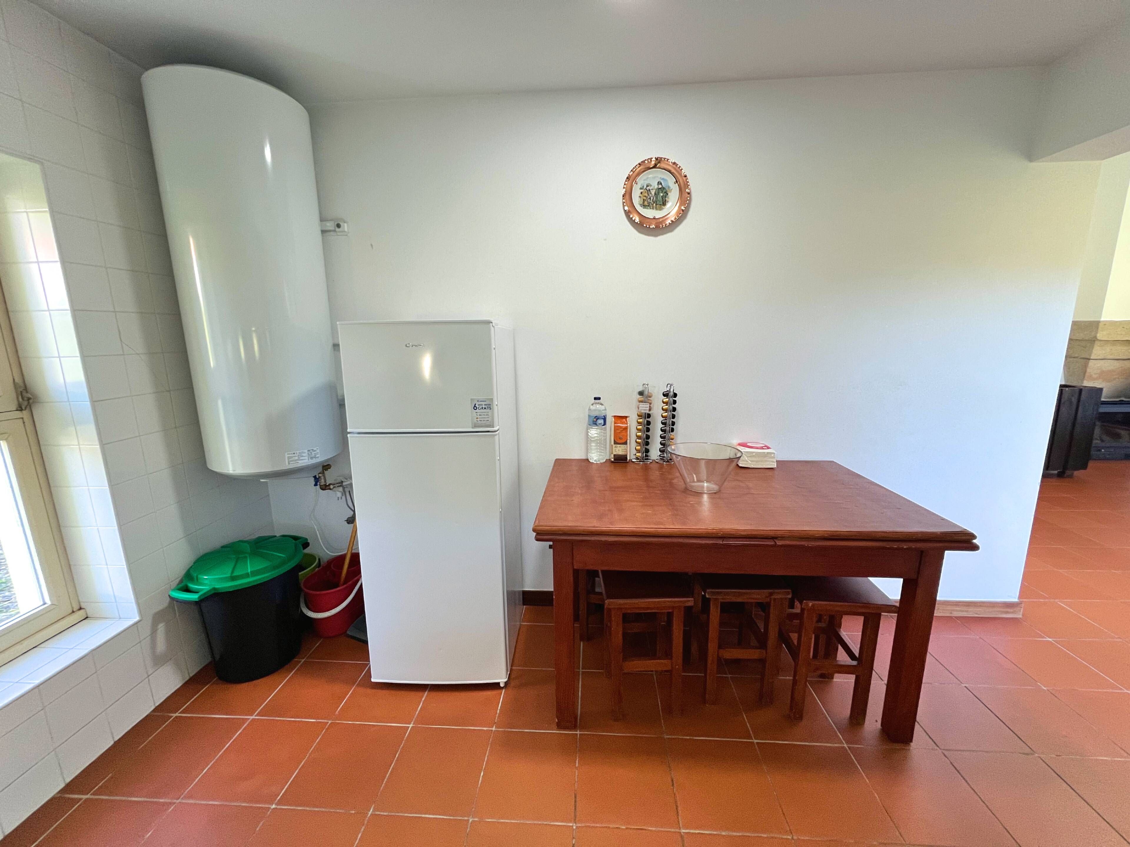 A kitchen with a white refrigerator, a wooden table with chairs, a green trash bin, and a water dispenser.