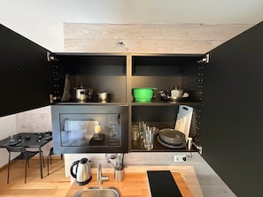 Kompakti keittiö, jossa on sisäänrakennettu uuni, pesuallas ja erilaisia keittiövälineitä.