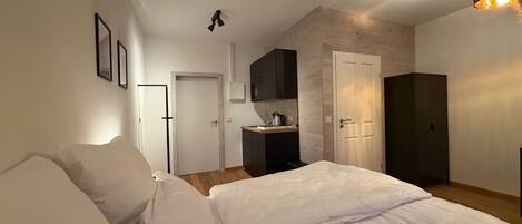 A bedroom with a bed, a kitchenette, and a door leading to another room.