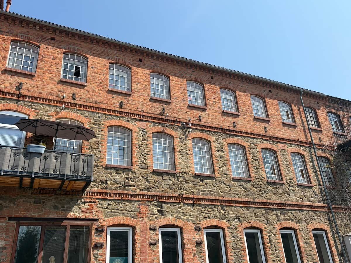 Ein mehrstöckiges Backsteingebäude mit Rundbogenfenstern und einem Balkon mit Metallgeländer.