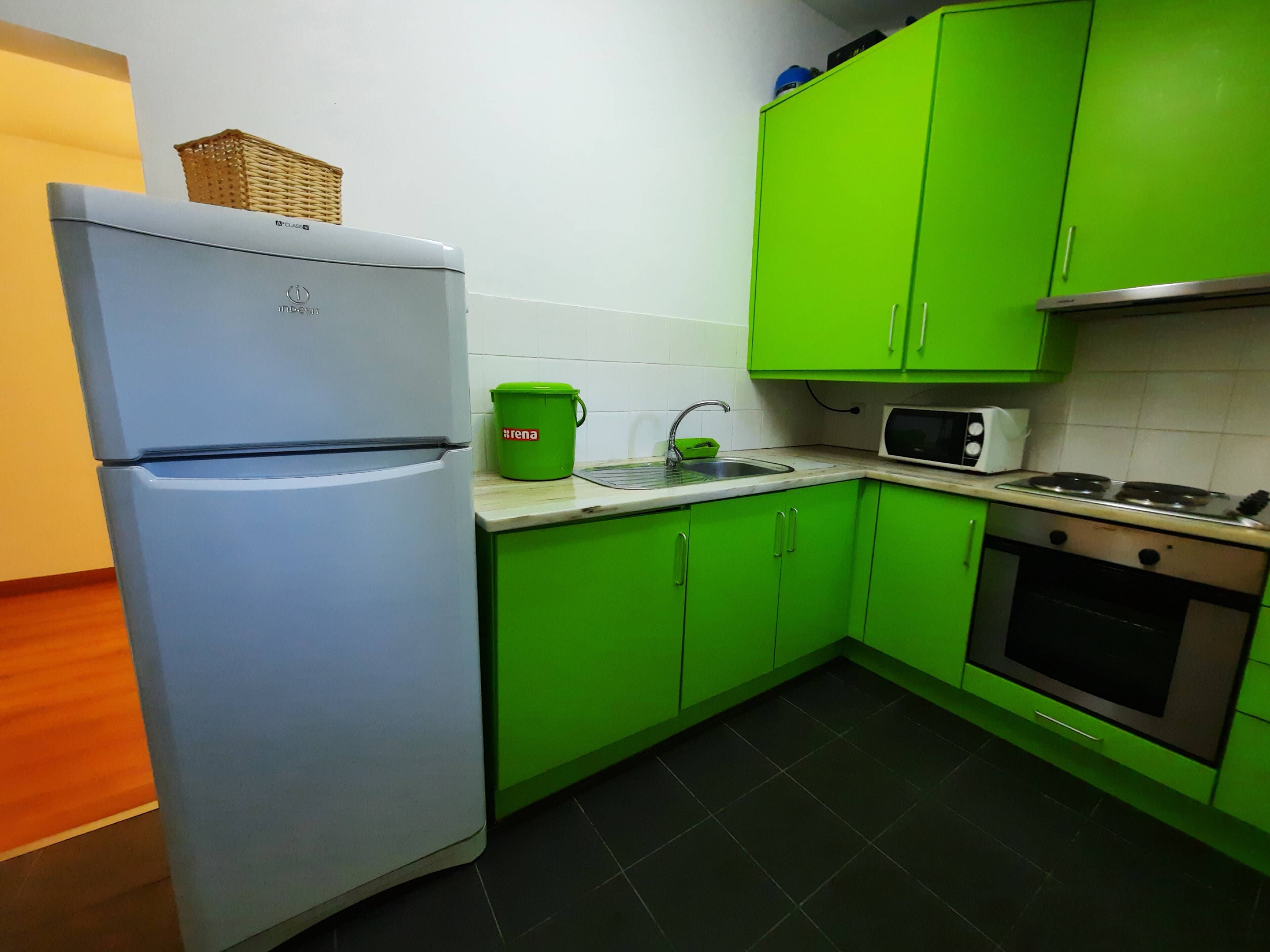 Una cocina con un refrigerador blanco, armarios verdes, un microondas y una estufa.