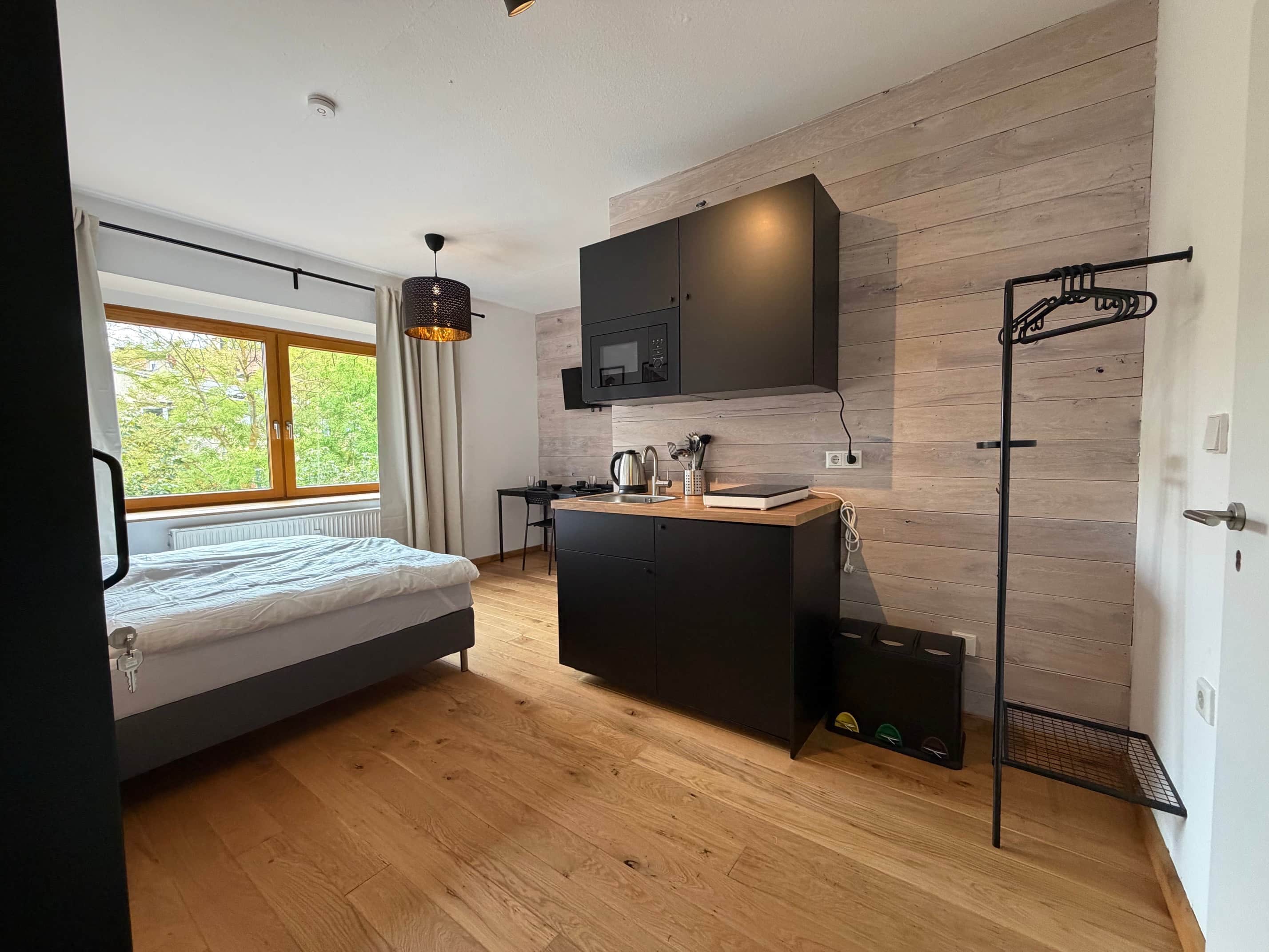 Une chambre moderne avec un lit, une petite kitchenette et une fenêtre avec des rideaux.