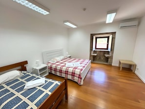 A bedroom with two beds, a stone wall, a window, and an air conditioning unit. - Rural Retreat Ponte de Lima (Ponte de Lima)