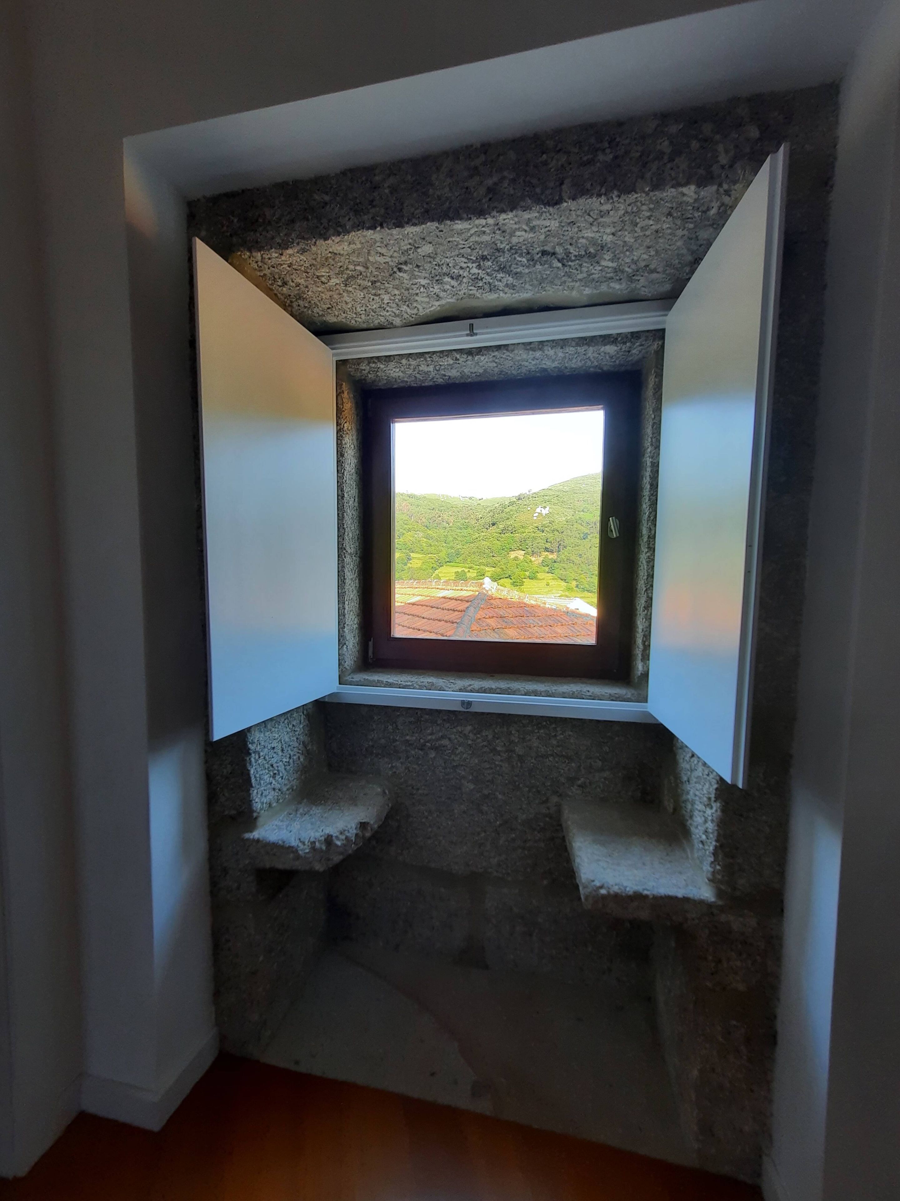 Ein kleines Zimmer mit Fensterblick auf eine grüne Landschaft.
