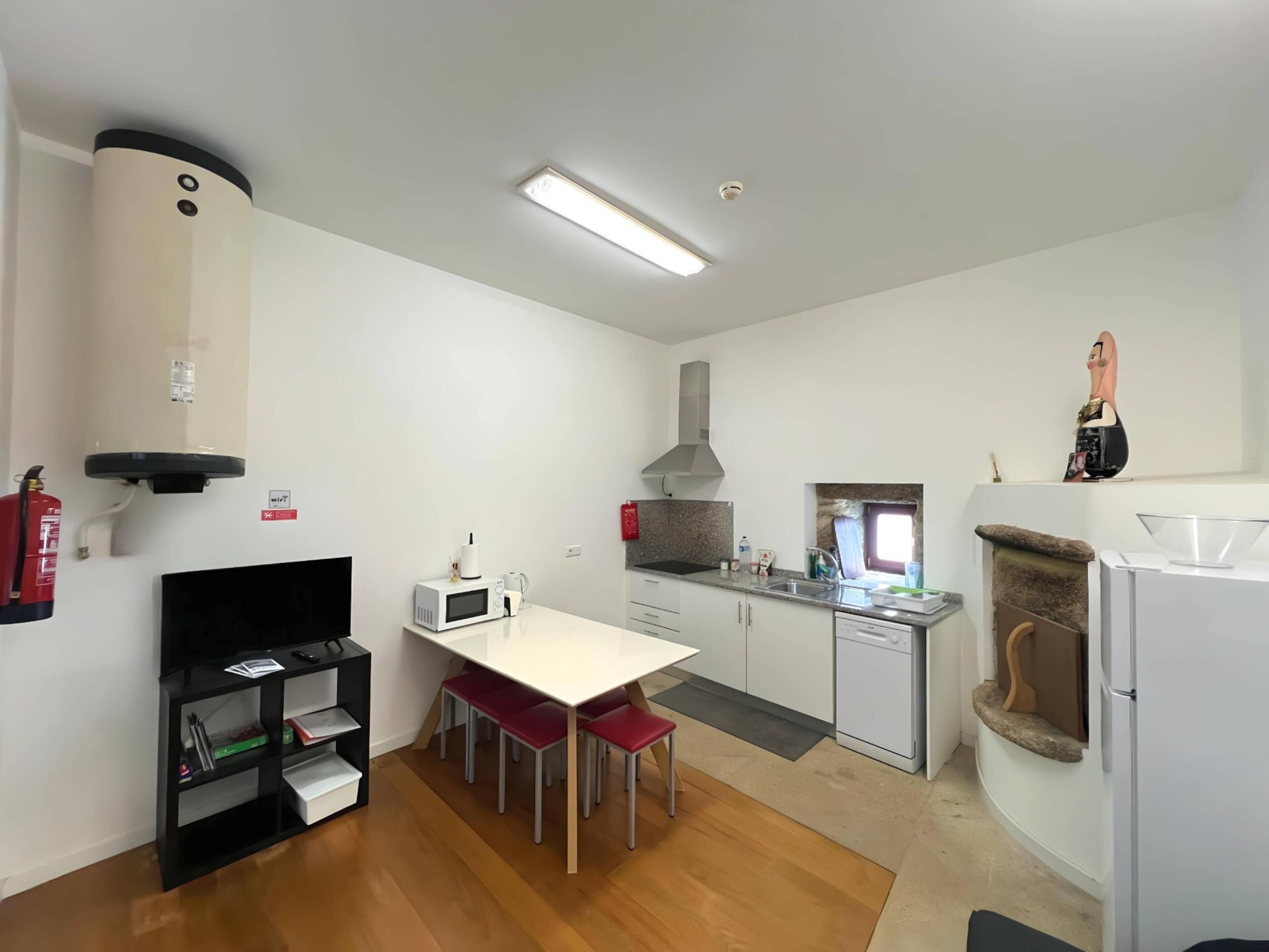 A modern kitchen with white cabinets, a microwave, a gas stove, and a dishwasher. There is a small dining area with a table and chairs.
