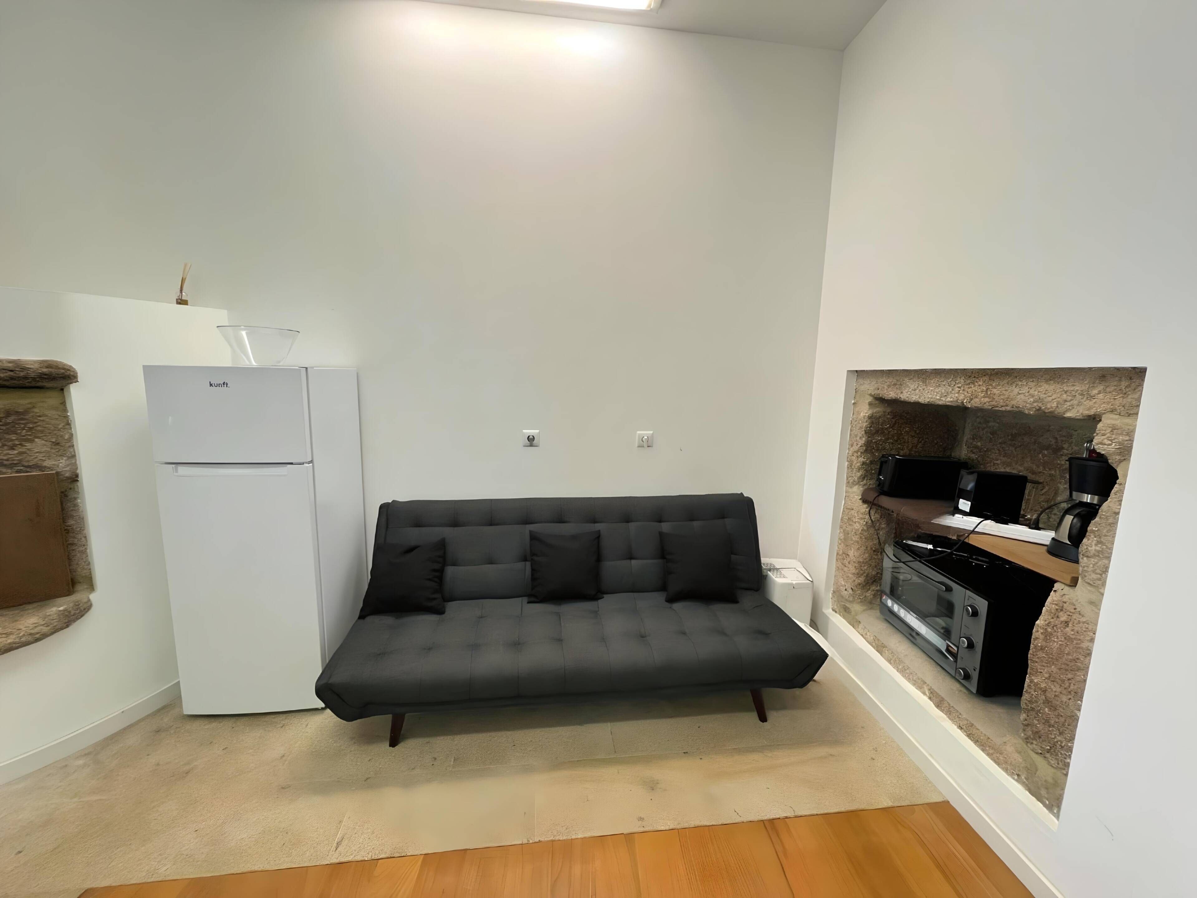 A compact living space with a sofa, a kitchenette, and a stone fireplace.