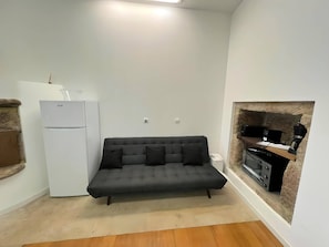 A compact living space with a sofa, a kitchenette, and a stone fireplace. - Rural Retreat Ponte de Lima (Ponte de Lima)