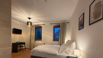 Ein Schlafzimmer mit einem Bett, einem Schreibtisch, einem Stuhl, einer Lampe und einem Fernseher an der Wand.