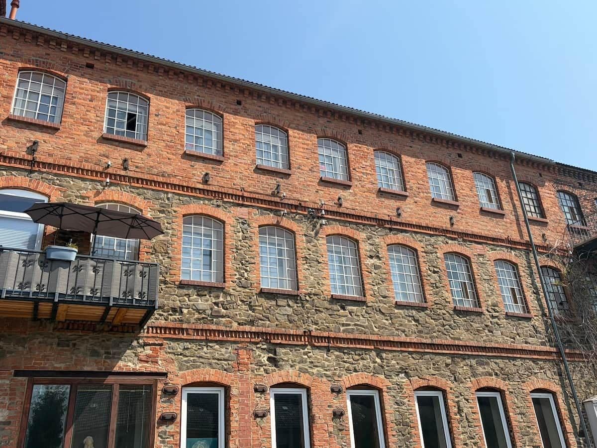 Ein mehrstöckiges Backsteingebäude mit Rundbogenfenstern und einem Balkon mit Metallgeländer.