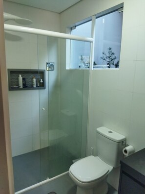 A bathroom with a glass-enclosed shower, a toilet, and a shelf with toiletries. - New Listing (Vera Cruz)