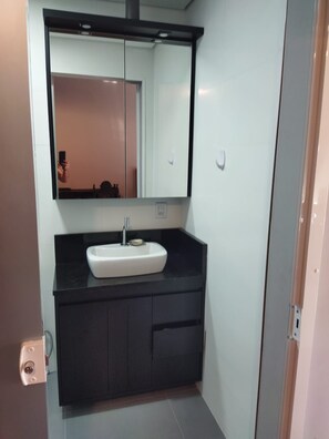 Een moderne badkamer met een witte wastafel, een donker aanrechtblad en een grote spiegel.