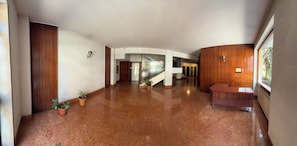A spacious hallway with a polished floor, wooden paneling on the walls, a reception desk, and potted plants. - New Listing (Roma)