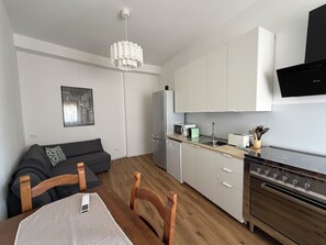 Cozinha moderna com forno embutido, micro-ondas e pia. Há uma mesa de jantar com cadeiras e um lustre.