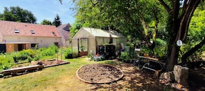 Ein Garten mit Gewächshaus, einer Holzbank und einem Baum.