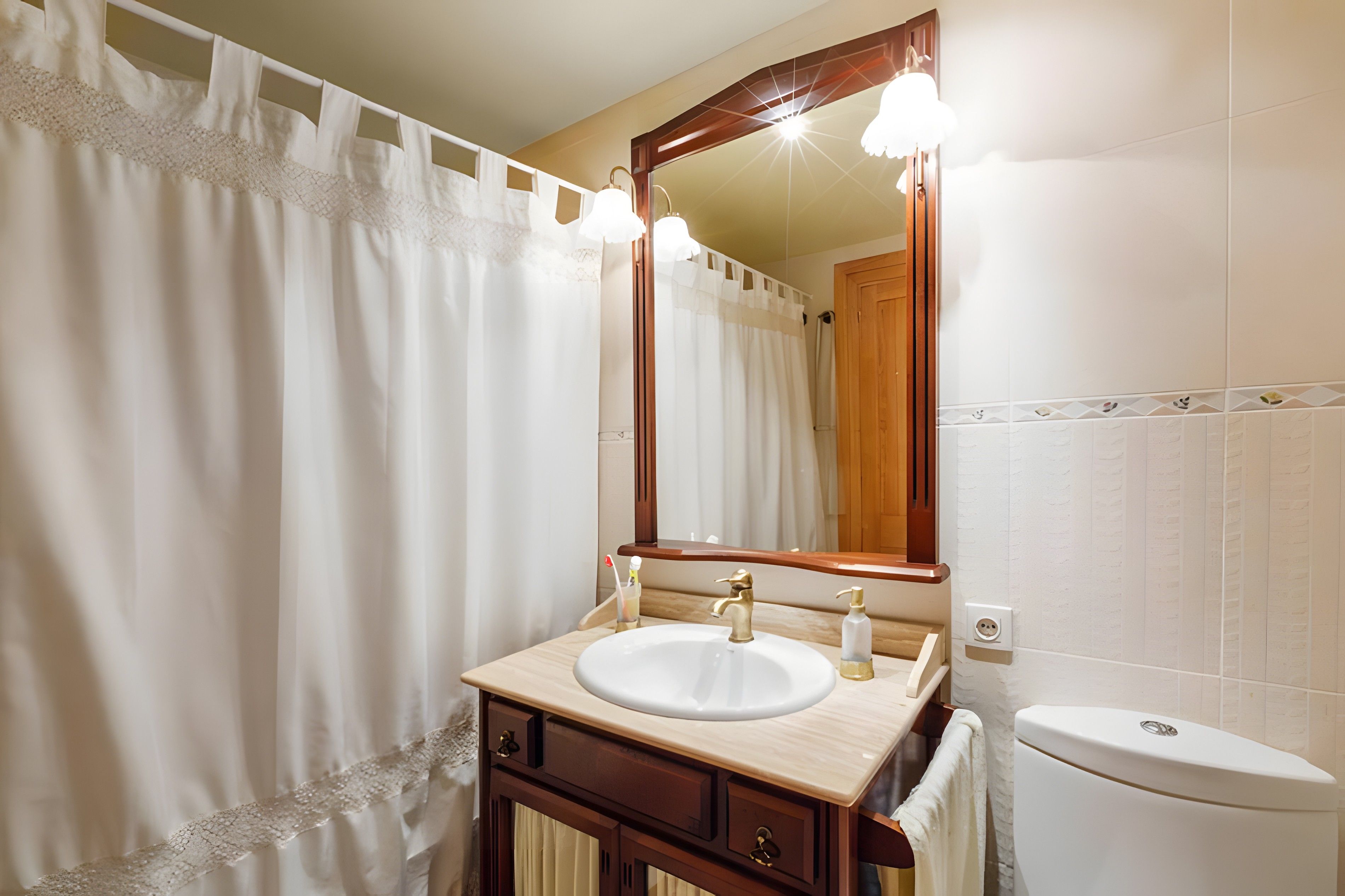A bathroom with a white sink, wooden vanity, a mirror, and a white toilet.