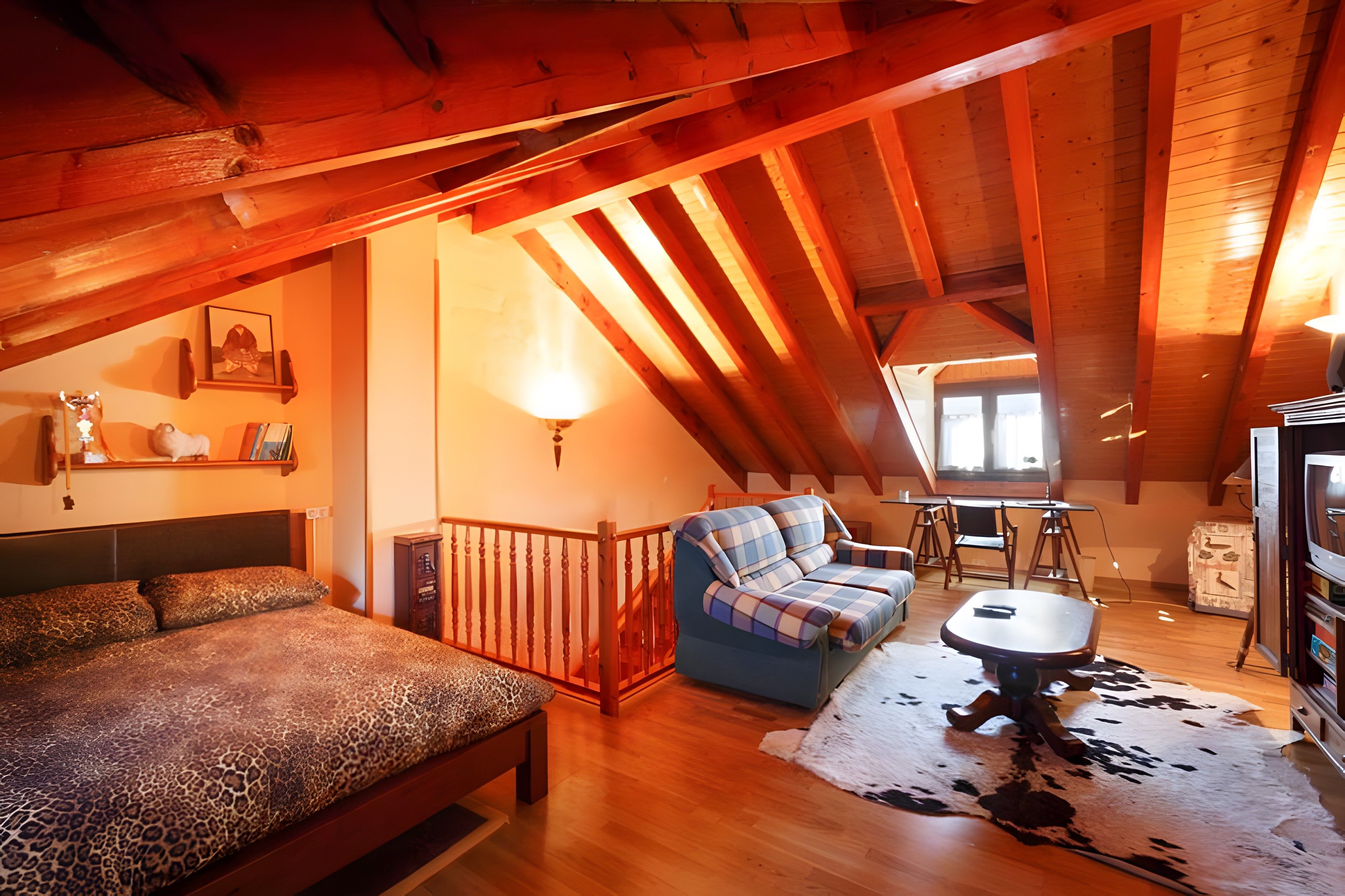 A cozy loft bedroom with a bed, a sofa, a small table, and a cowhide rug.