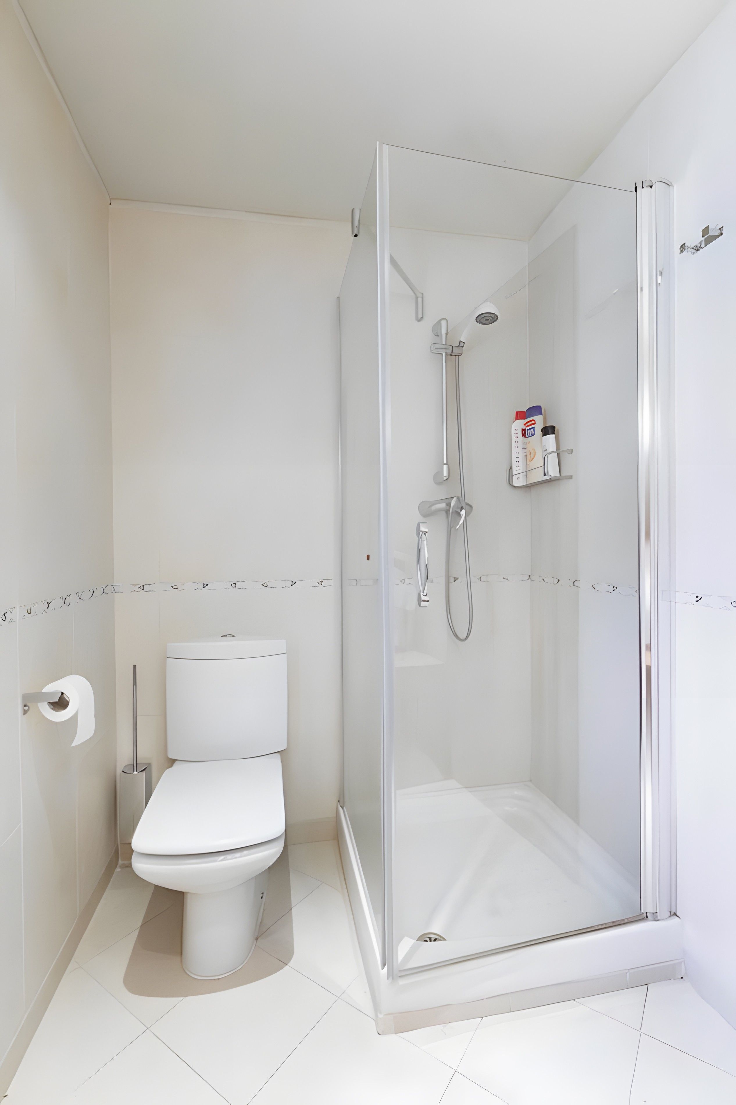 Un baño moderno con inodoro, cabina de ducha con mampara de vidrio y estante con artículos de aseo.