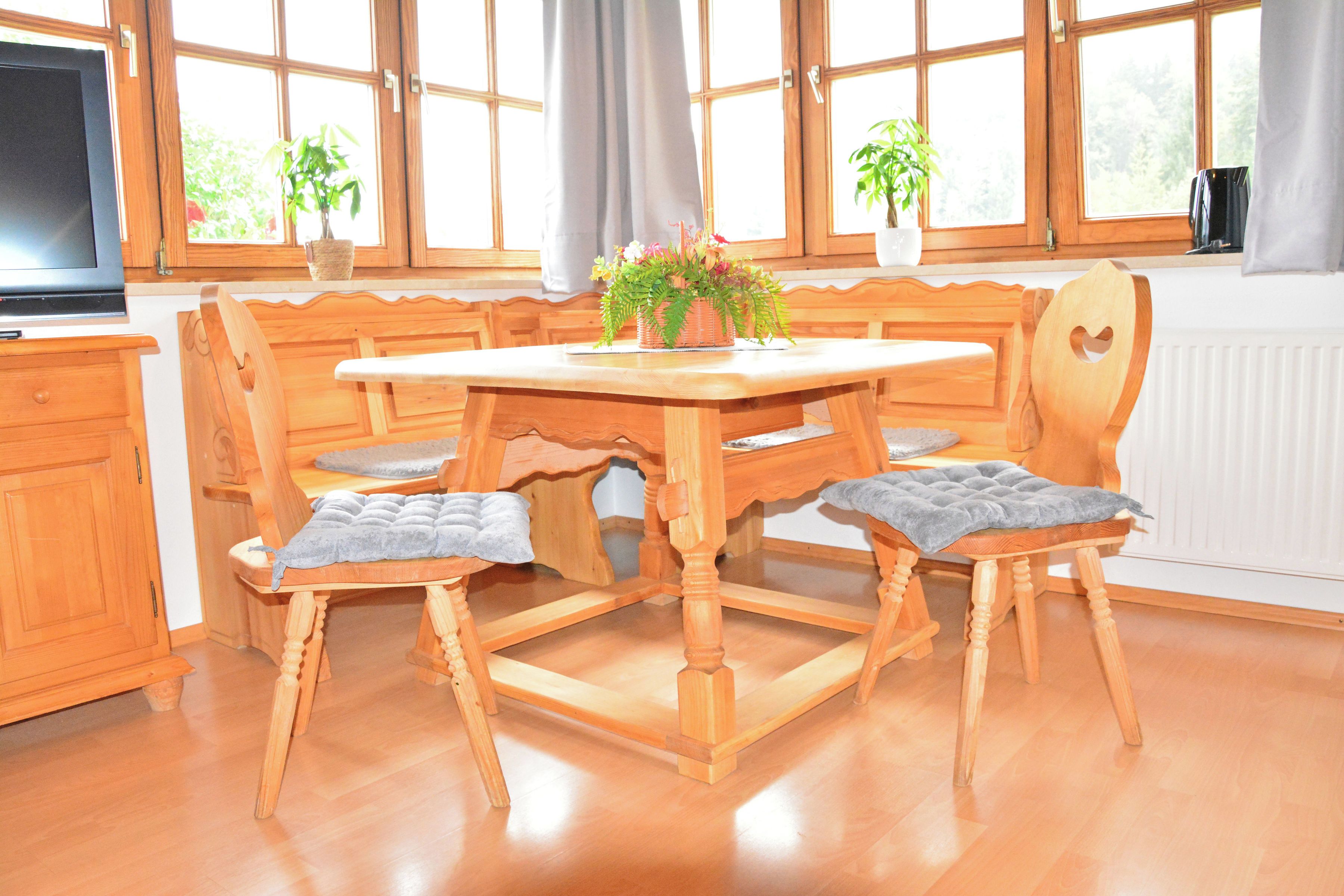 A wooden dining table with four chairs, a television, and two potted plants.