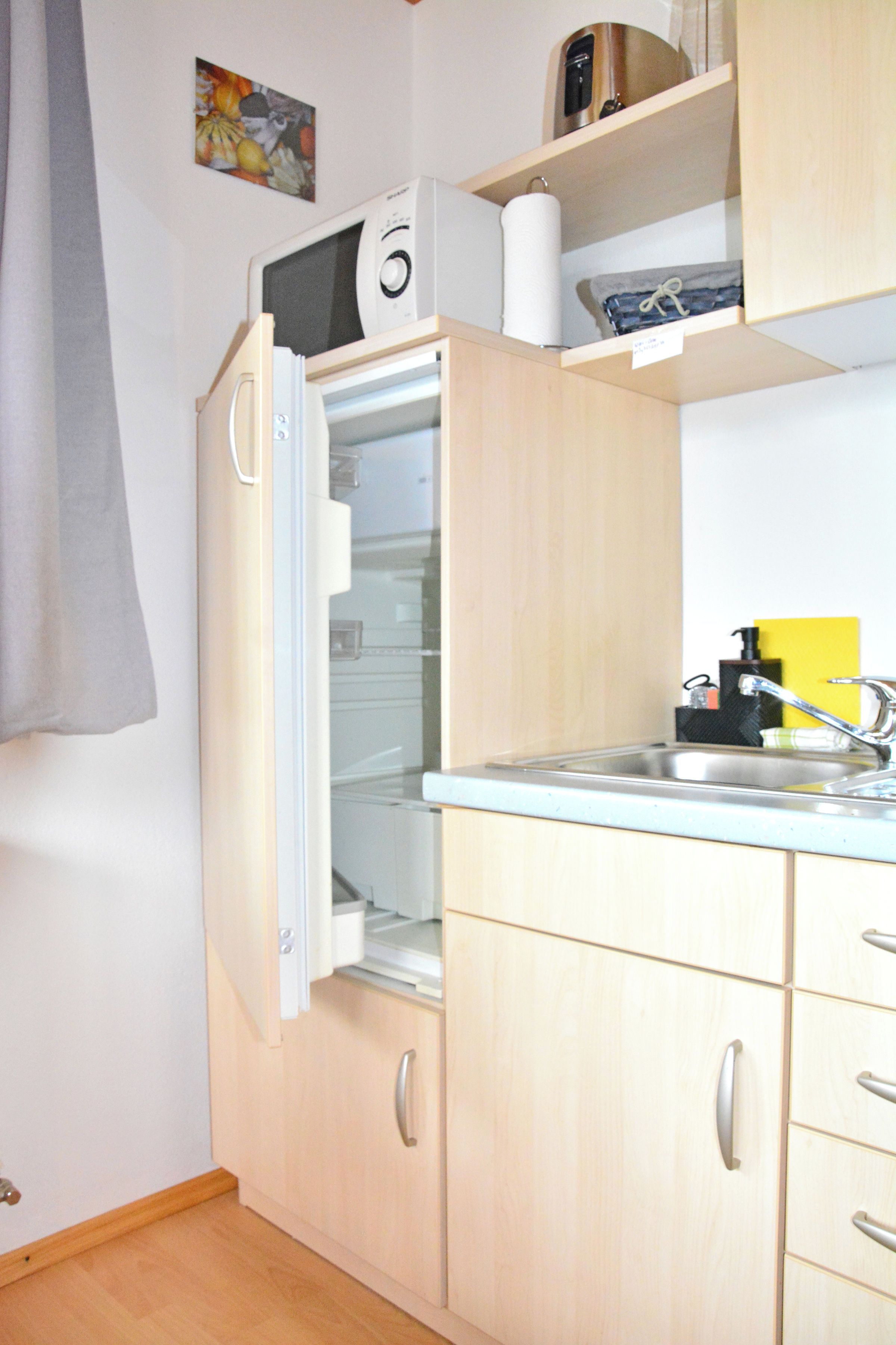 Une cuisine compacte dotée d’un réfrigérateur encastré, d’un évier et d’armoires en bois.