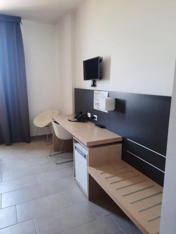 Una habitación de hotel pequeña y moderna con un escritorio de madera, una silla, un televisor de pantalla plana montado en la pared y un mueble blanco pequeño.
