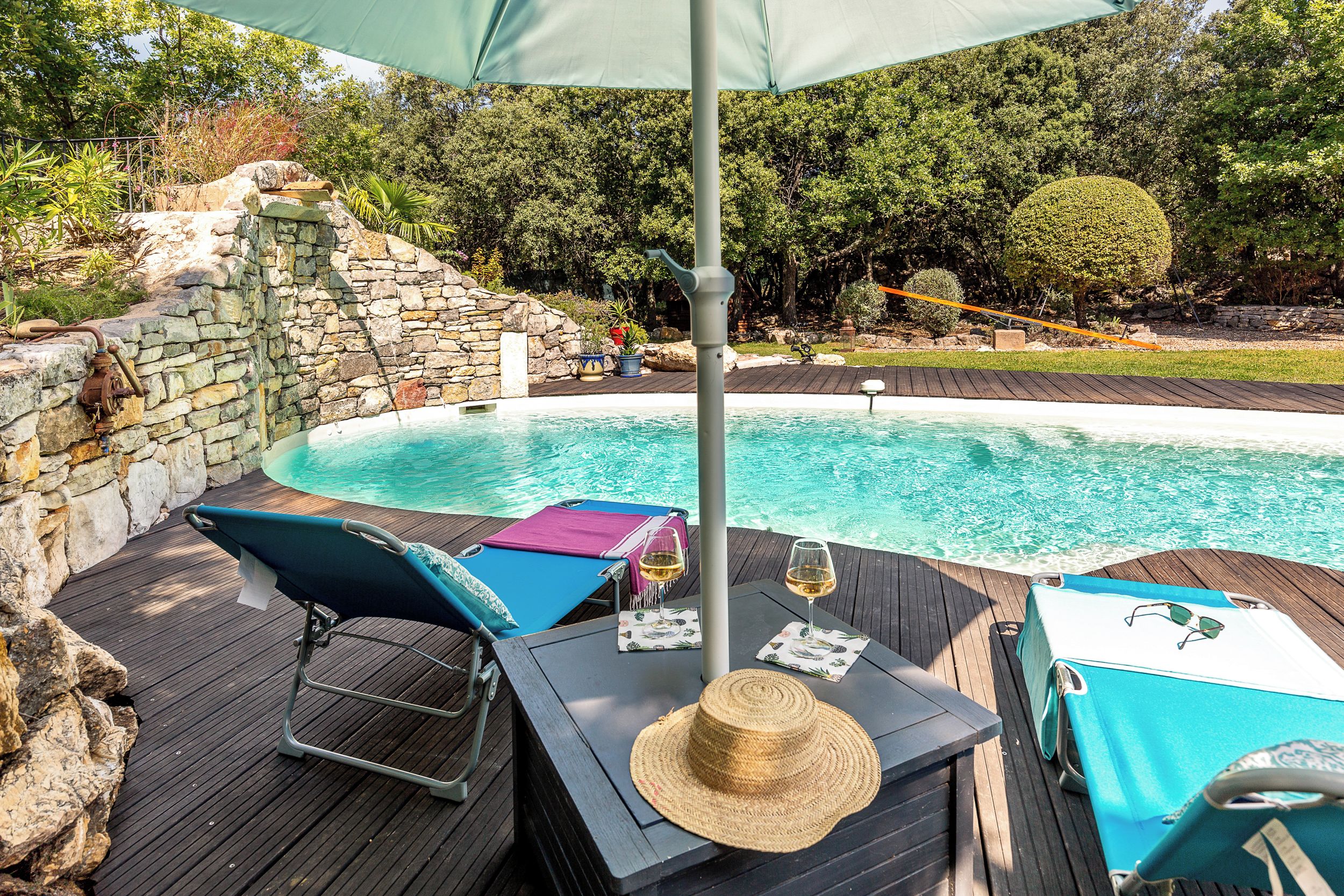 A poolside area with a stone wall, lounge chairs, and a table with a drink.
