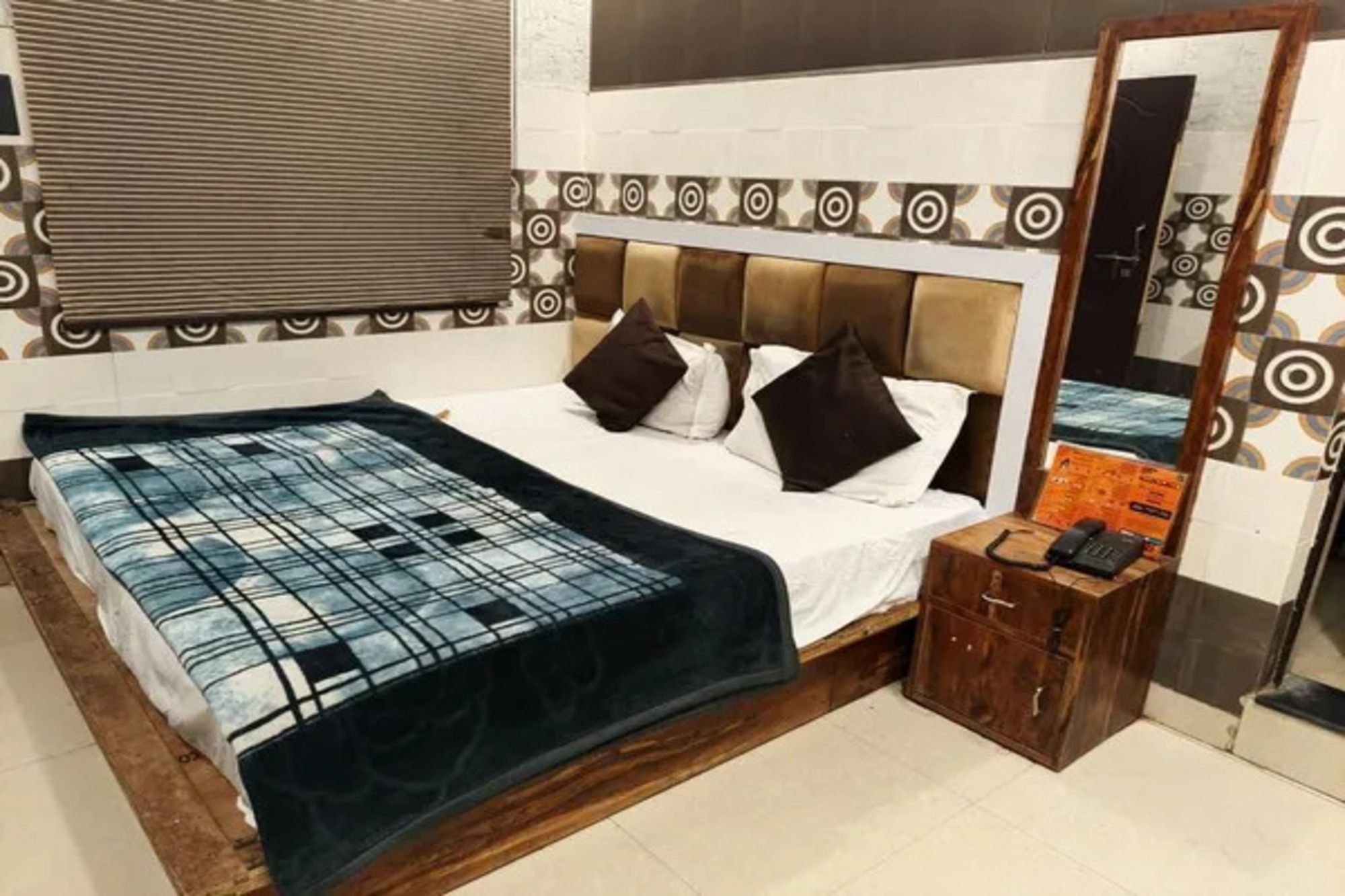 A bedroom with a bed, a bedside table, a mirror, and a patterned wall.