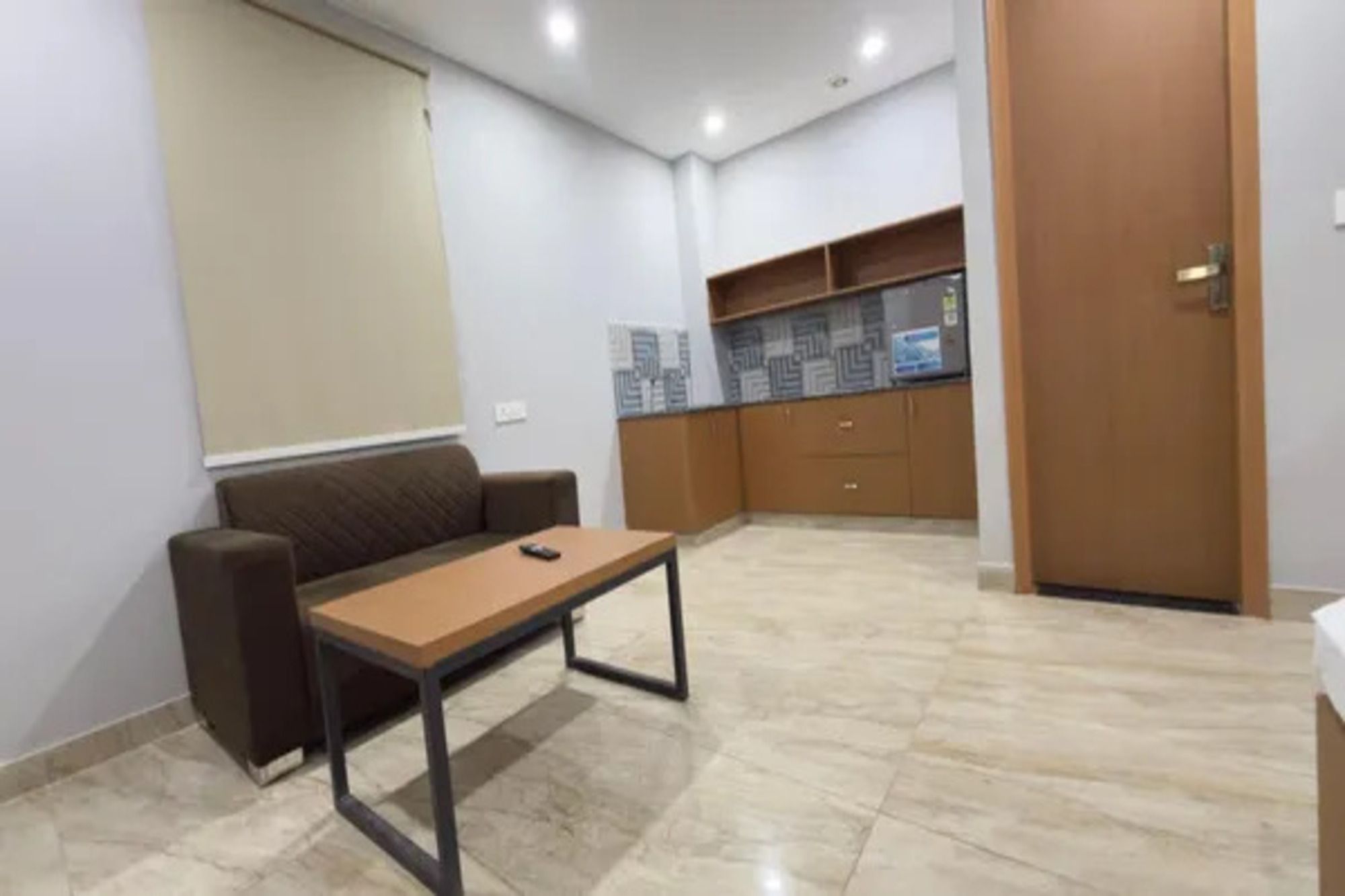 Una habitación con sofá, mesa, zona de cocina con armarios y una puerta.