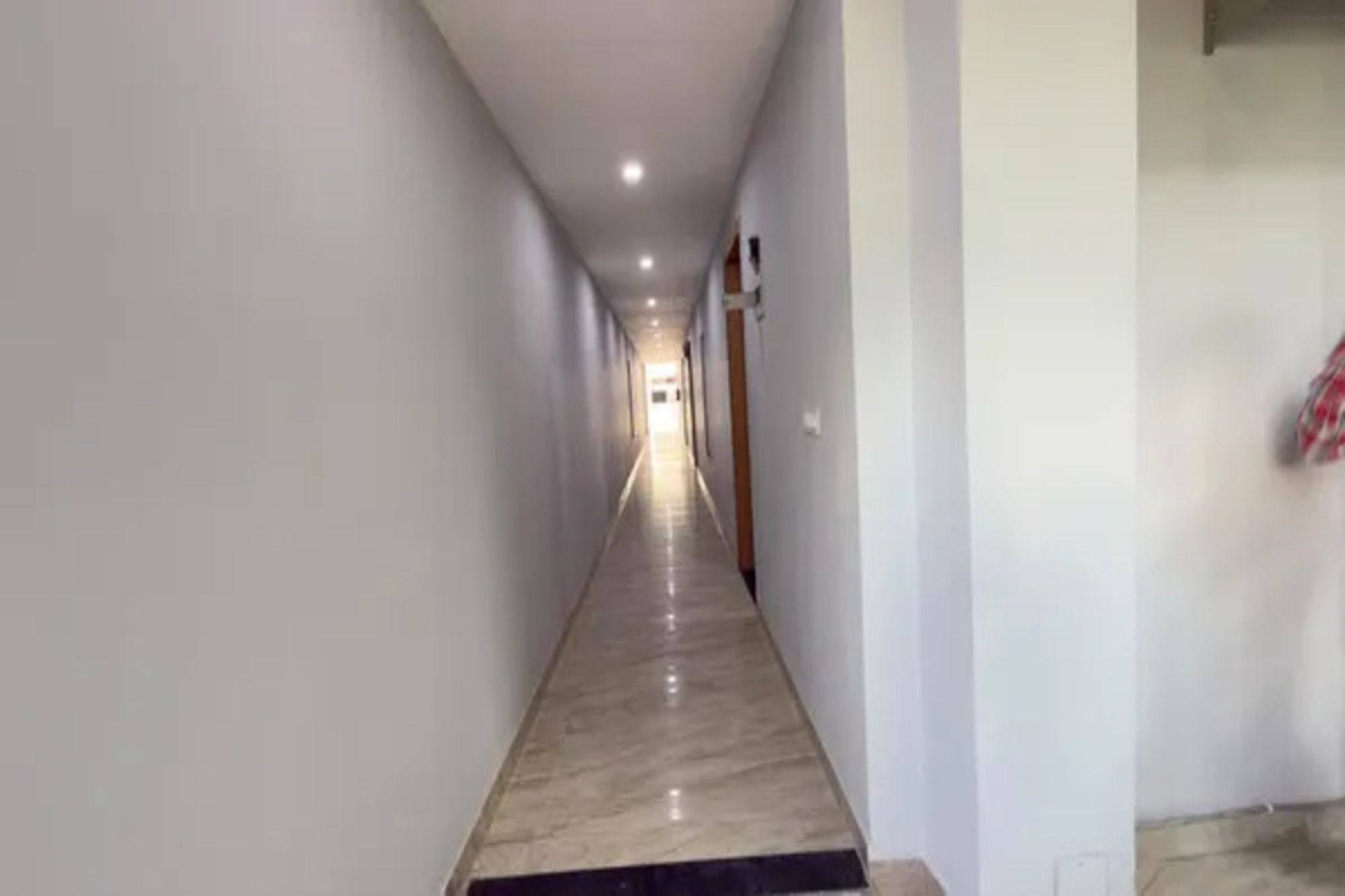 Un pasillo largo y estrecho con piso pulido, paredes blancas y una puerta al final.