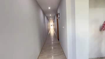 Un long couloir étroit, doté d’un sol ciré, de murs blancs et d’une porte au fond.