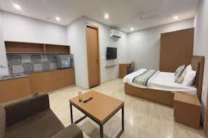 A compact hotel room with a bed, a small table, a sofa, a kitchenette, and a TV. - FabHotel Prime Grihum 128 (Noida)