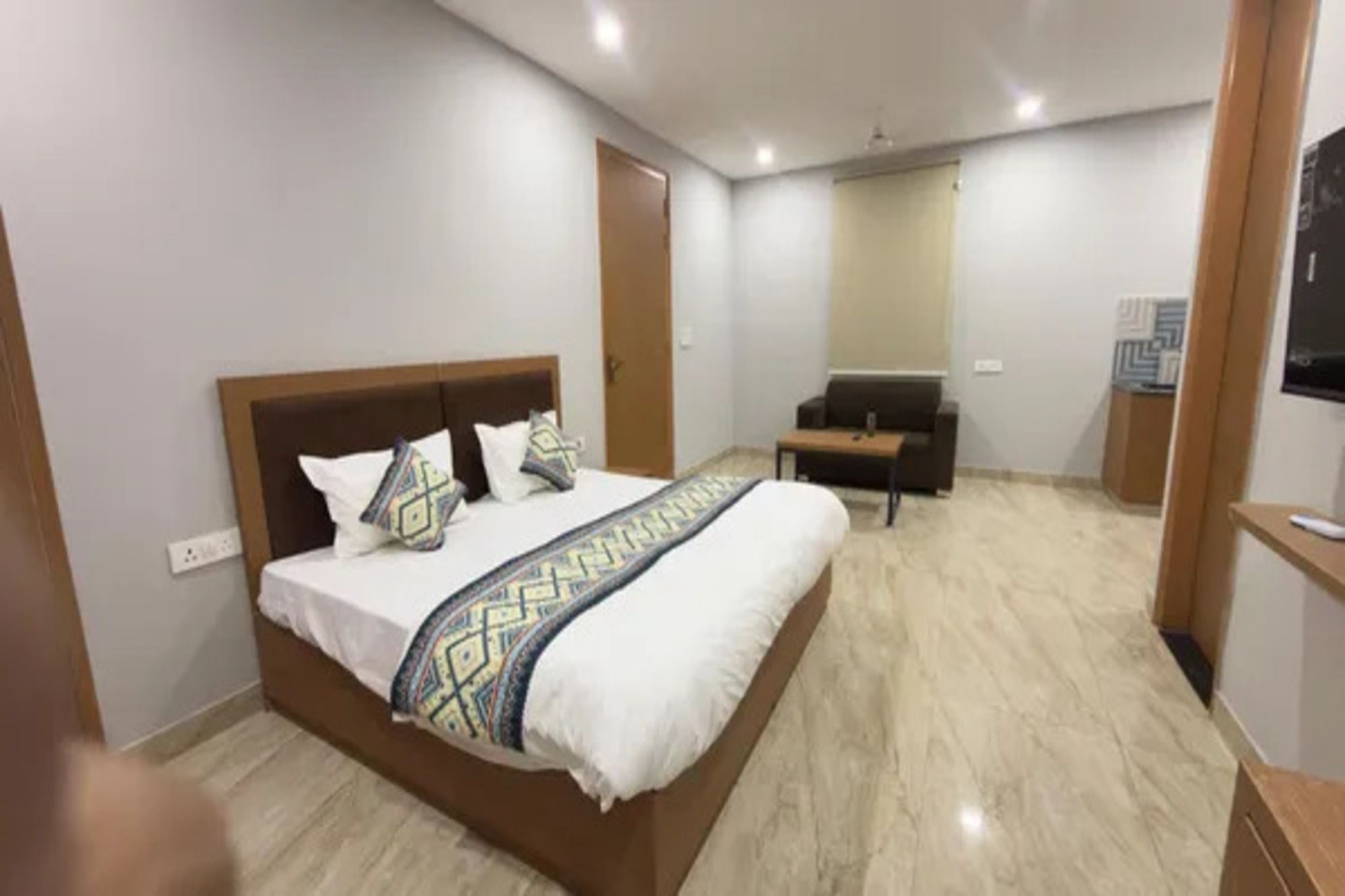 A hotel room with a large bed, a sofa, a TV, and a mirror.