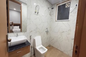 A bathroom with a marble wall, a sink, a toilet, and a shower area. - FabHotel Prime Grihum 128 (Noida)