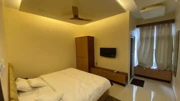 Ein modernes Schlafzimmer mit Bett, Schrank, Fernseher und einem Badezimmer mit Vorhängen.