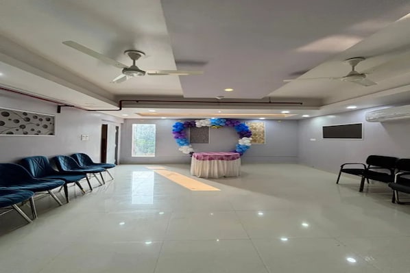 Amplia habitación con mostrador de recepción, sillas, ventiladores de techo y un arco decorativo de globos.