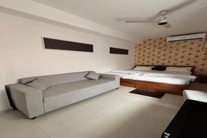 A bedroom with a grey sofa, a bed with white bedding, a ceiling fan, and an air conditioning unit. - FabHotel RM Royale (Bhubaneswar)