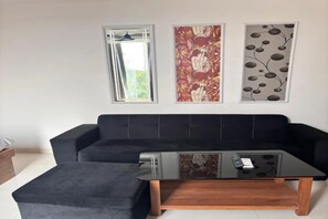 Una sala de estar moderna con un sofá negro, una mesa de centro de vidrio y tres obras de arte enmarcadas en la pared.