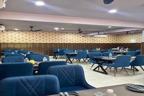 Un salón de conferencias con filas de sillas azules, mesas, ventiladores de techo y una pared con diseño.